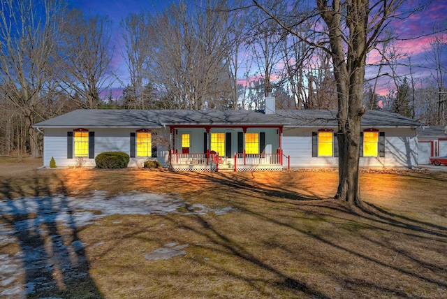 view of front of house featuring covered porch, a chimney, and a lawn