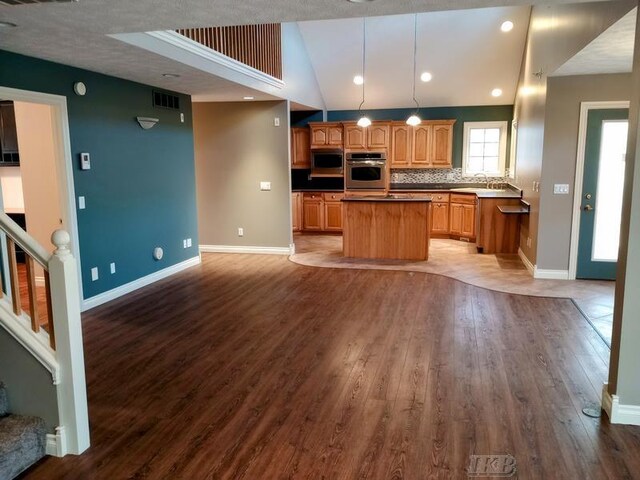 kitchen with a center island, open floor plan, appliances with stainless steel finishes, wood finished floors, and a sink