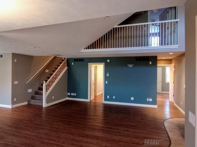 unfurnished living room with visible vents, baseboards, stairway, wood finished floors, and high vaulted ceiling