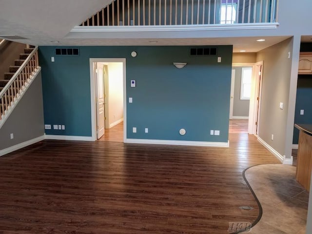 unfurnished living room featuring wood finished floors, a high ceiling, baseboards, and visible vents