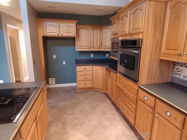 kitchen with light tile patterned floors, light brown cabinets, baseboards, appliances with stainless steel finishes, and dark countertops