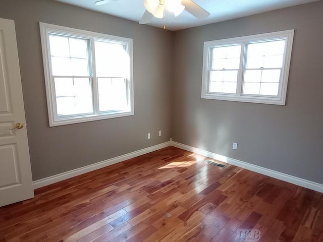 unfurnished room with ceiling fan, wood finished floors, visible vents, and baseboards