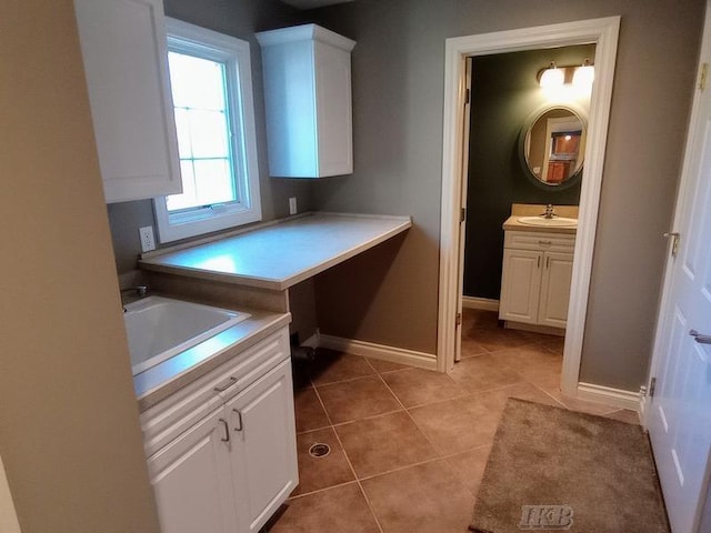 interior space featuring light tile patterned flooring, white cabinets, baseboards, and a sink