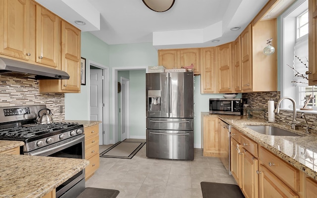 kitchen featuring light brown cabinetry, under cabinet range hood, light stone counters, a sink, and stainless steel appliances