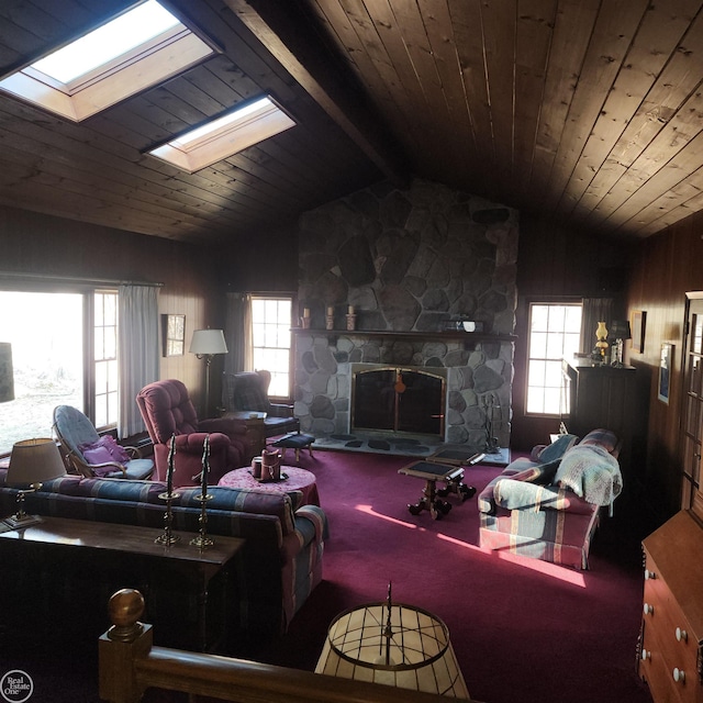 carpeted living area featuring a stone fireplace, vaulted ceiling with skylight, wooden ceiling, and wooden walls