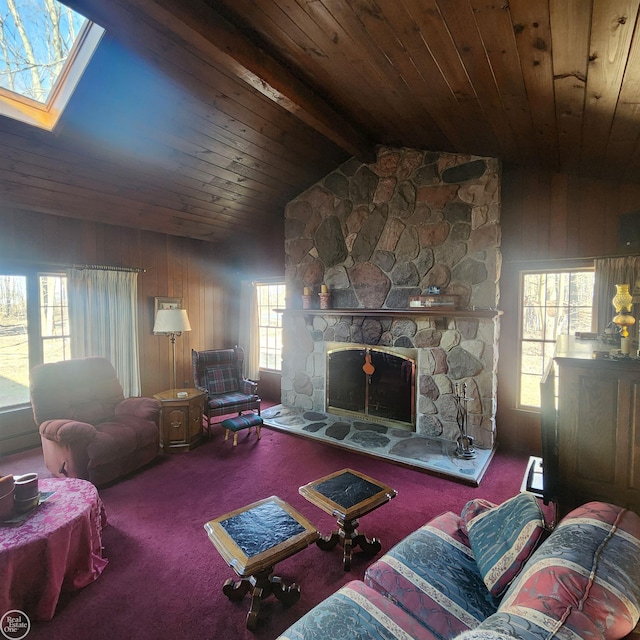 living area featuring vaulted ceiling with skylight, a stone fireplace, carpet flooring, and a healthy amount of sunlight