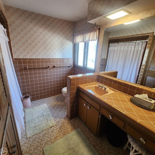 bathroom with wallpapered walls, tile walls, a wainscoted wall, toilet, and vanity