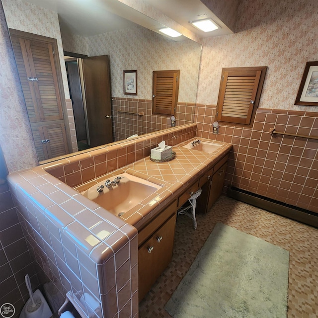 bathroom with a sink, a wainscoted wall, and wallpapered walls