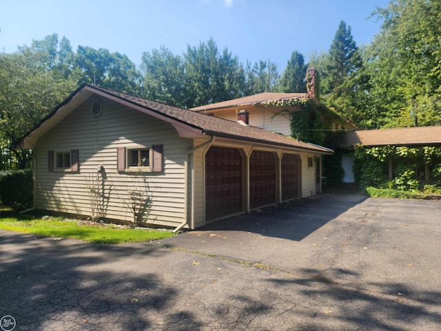 view of property exterior featuring aphalt driveway, an attached garage, and a chimney