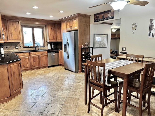 kitchen featuring dark countertops, backsplash, brown cabinets, stainless steel appliances, and a sink