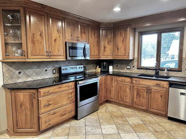 kitchen featuring dark countertops, tasteful backsplash, appliances with stainless steel finishes, brown cabinetry, and a sink