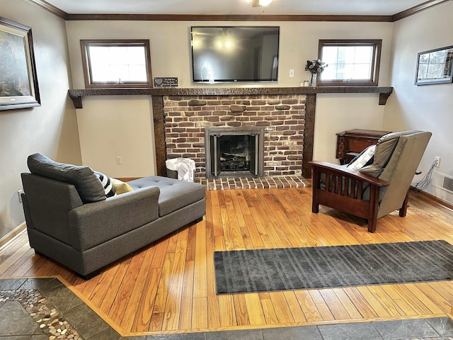 living area featuring crown molding, a brick fireplace, baseboards, and wood-type flooring