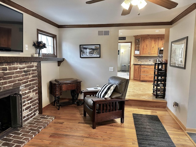 living area featuring visible vents, a brick fireplace, baseboards, ornamental molding, and light wood-style flooring