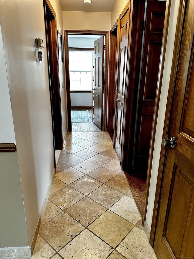 corridor with baseboards and stone tile floors