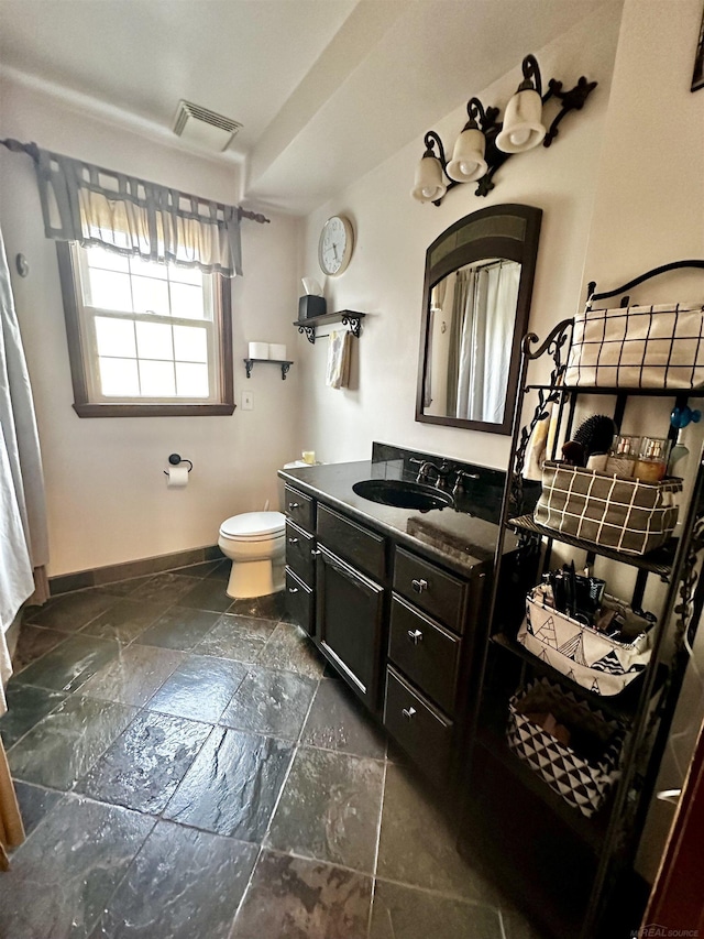 bathroom featuring vanity, stone tile floors, visible vents, baseboards, and toilet