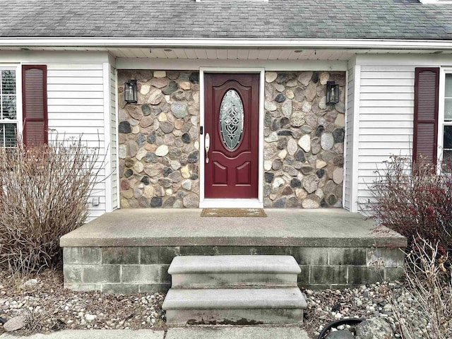 entrance to property featuring stone siding and roof with shingles