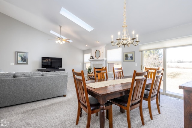 carpeted dining room featuring high vaulted ceiling, a skylight, a fireplace, and ceiling fan with notable chandelier