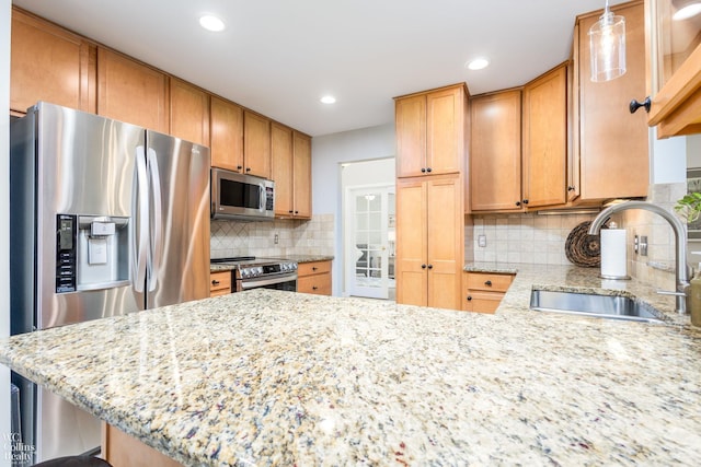 kitchen featuring a sink, backsplash, stainless steel appliances, a peninsula, and light stone countertops