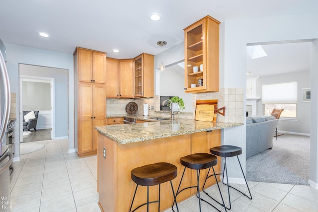 kitchen with glass insert cabinets, light stone countertops, a breakfast bar, a peninsula, and a sink