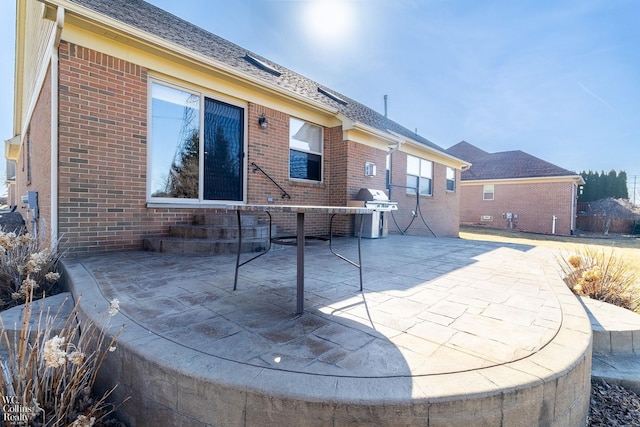 rear view of property with brick siding, a patio area, and a shingled roof