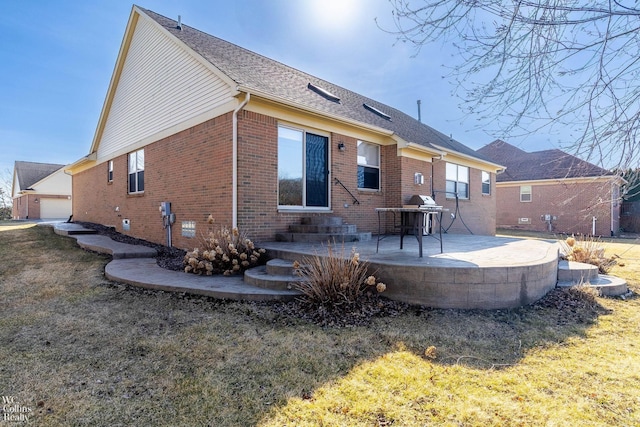 back of house featuring brick siding, a lawn, a patio, and roof with shingles