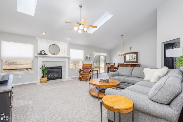 living room featuring carpet flooring, ceiling fan with notable chandelier, a tile fireplace, and a skylight