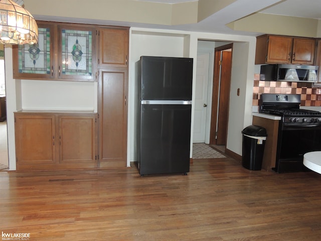 kitchen with backsplash, black appliances, brown cabinetry, and light wood finished floors