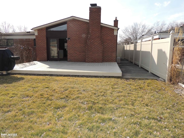 back of house featuring a yard, brick siding, a chimney, and fence