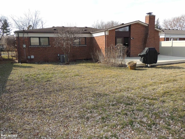 rear view of property featuring a patio, brick siding, a lawn, and fence