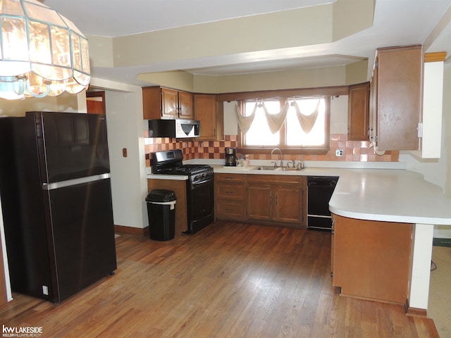 kitchen featuring wood finished floors, a sink, black appliances, light countertops, and brown cabinets