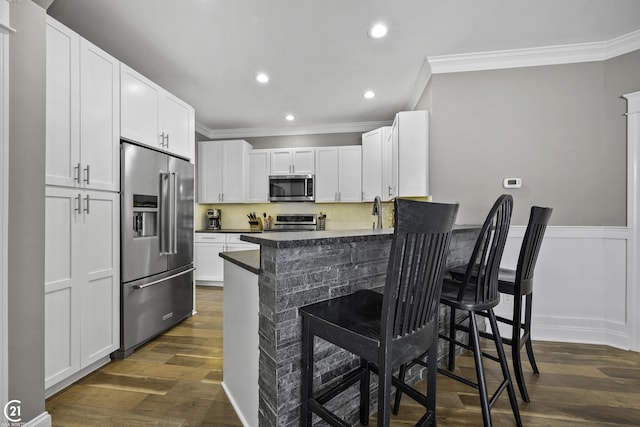 kitchen featuring dark wood-style floors, stainless steel appliances, crown molding, and a breakfast bar