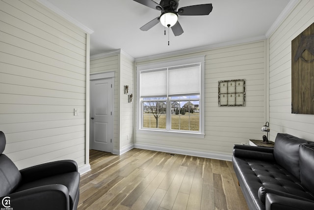 living area with wood finished floors, visible vents, baseboards, ceiling fan, and ornamental molding