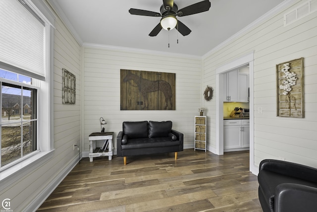 sitting room with a ceiling fan, baseboards, dark wood-style floors, visible vents, and ornamental molding