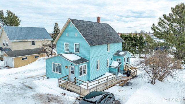 snow covered house with a deck, a shingled roof, and a chimney