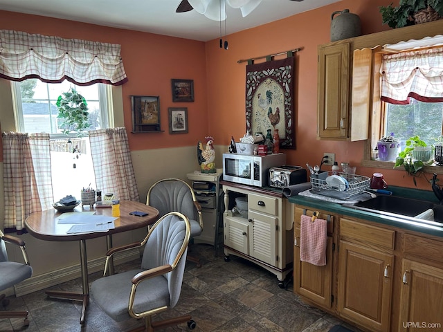 kitchen featuring brown cabinets, a ceiling fan, stone finish floor, a sink, and stainless steel microwave