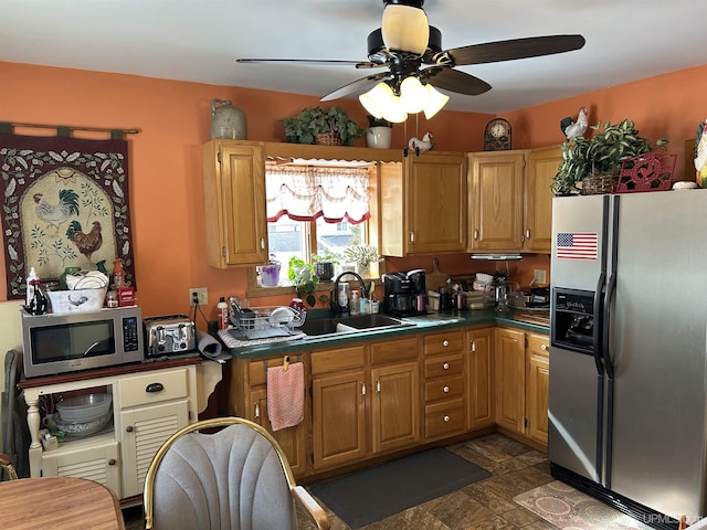 kitchen with a ceiling fan, a sink, stone finish flooring, dark countertops, and appliances with stainless steel finishes