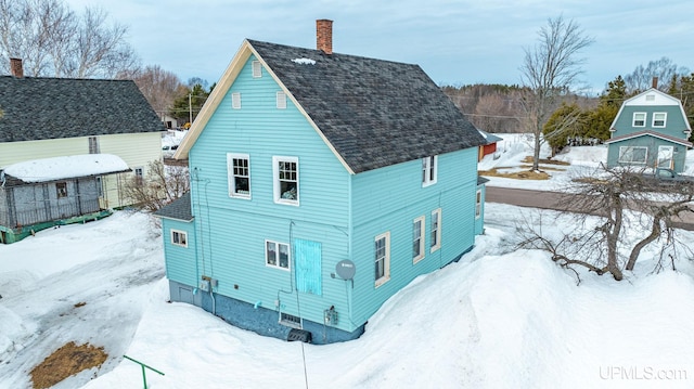 view of snow covered exterior with a chimney, an outdoor structure, and a shingled roof