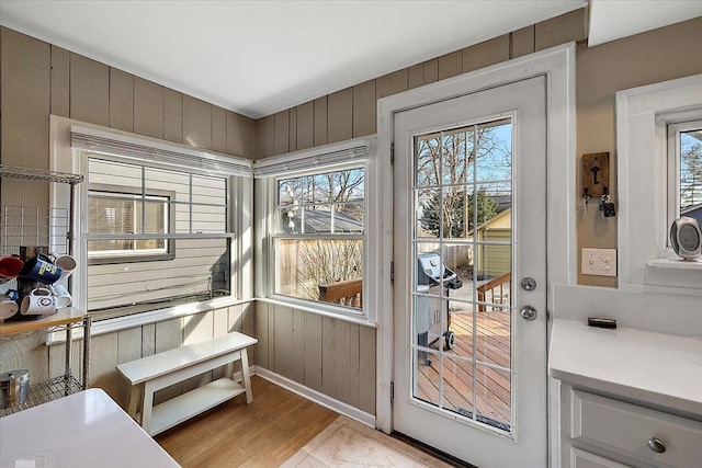 doorway to outside featuring wooden walls, light wood-type flooring, and baseboards