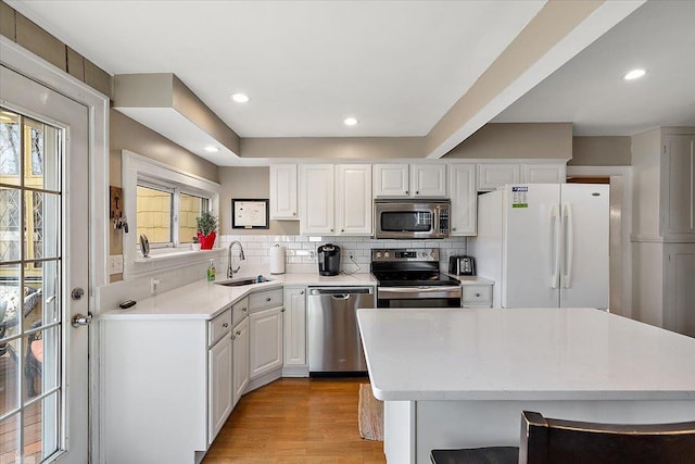 kitchen featuring backsplash, light wood-type flooring, stainless steel appliances, white cabinetry, and a sink