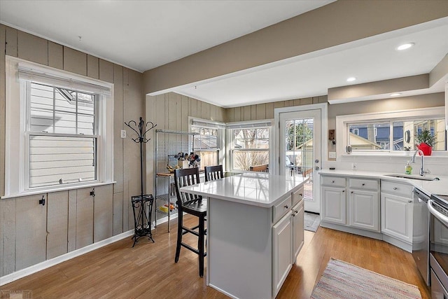 kitchen with a kitchen bar, a sink, a kitchen island, light wood-style floors, and light countertops