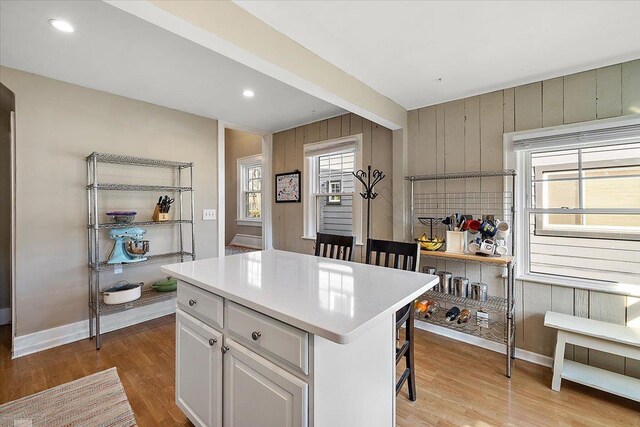 kitchen with light wood-type flooring, a breakfast bar, a kitchen island, wooden walls, and light countertops