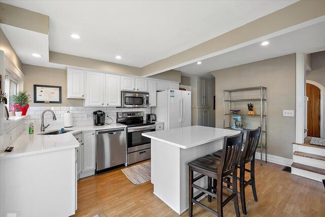 kitchen featuring a breakfast bar area, light wood-style flooring, a sink, decorative backsplash, and stainless steel appliances