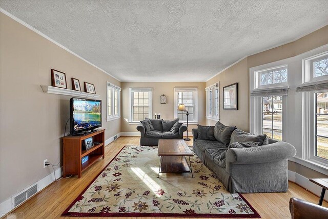 living area featuring visible vents, baseboards, light wood-style floors, and ornamental molding