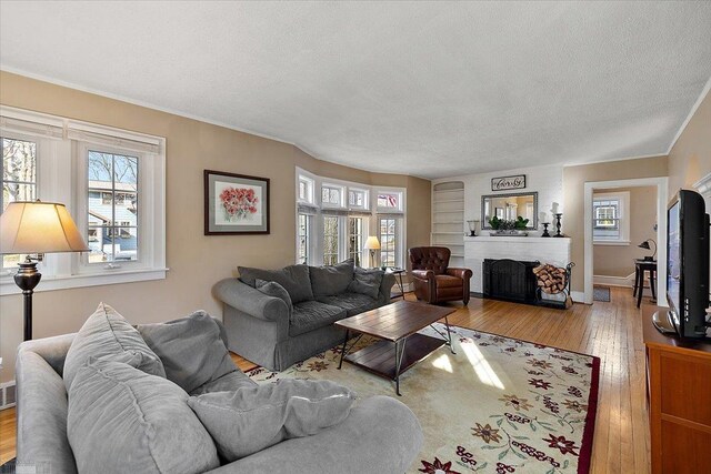 living area with baseboards, a textured ceiling, a fireplace, and hardwood / wood-style flooring