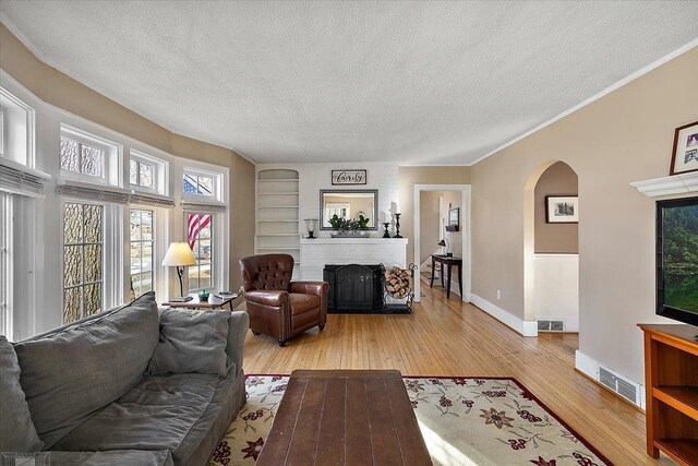 living room with a textured ceiling, arched walkways, light wood finished floors, baseboards, and a brick fireplace