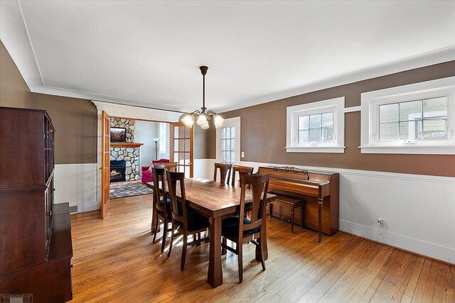 dining area featuring a wainscoted wall, a stone fireplace, a chandelier, and light wood-style flooring