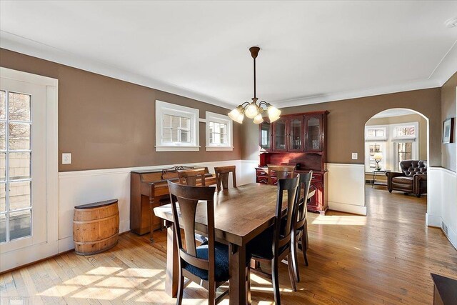 dining room featuring a notable chandelier, arched walkways, light wood finished floors, and ornamental molding