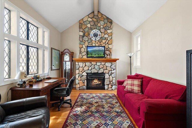 office space with a stone fireplace, vaulted ceiling with beams, and wood finished floors