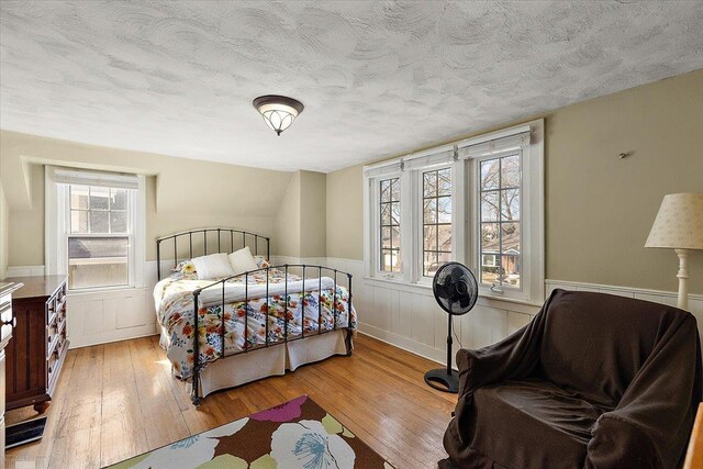 bedroom featuring hardwood / wood-style flooring, wainscoting, and a textured ceiling