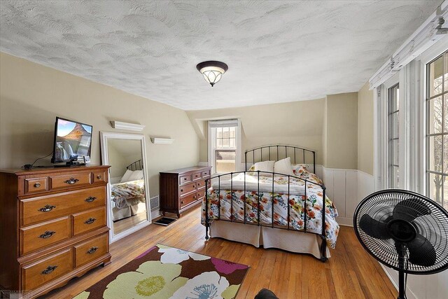 bedroom featuring light wood-type flooring, a textured ceiling, and wainscoting